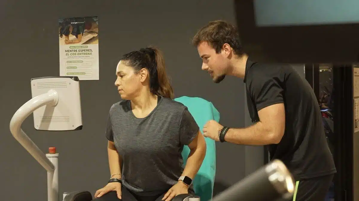 Entrenador de Energie Fitness acompañando a una socia en una máquina guiada